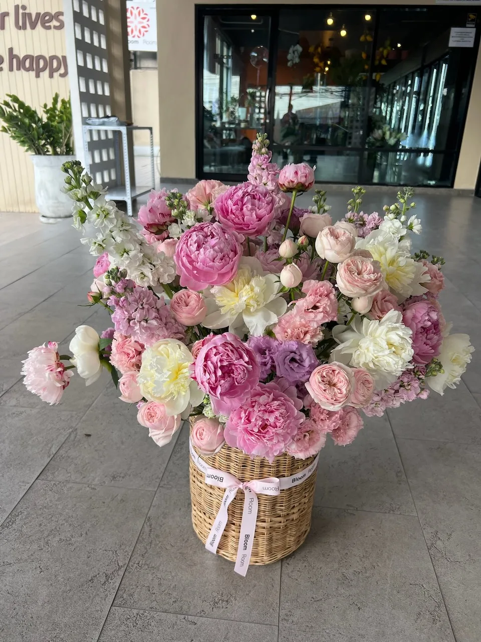 Tall pastel pink basket arrangement positioned outside the Bloom Room storefront