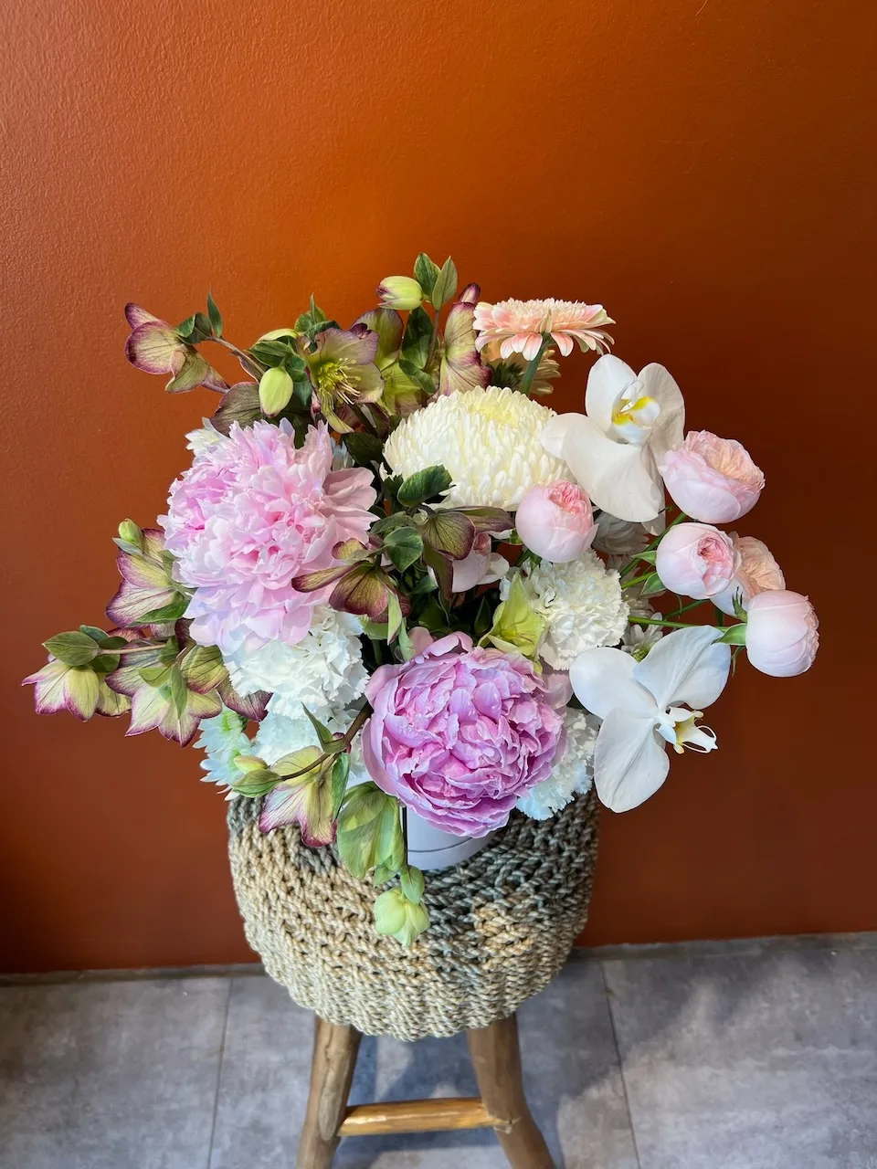 Pastel arrangement with pink peonies, white orchids and dahlias in woven rattan basket