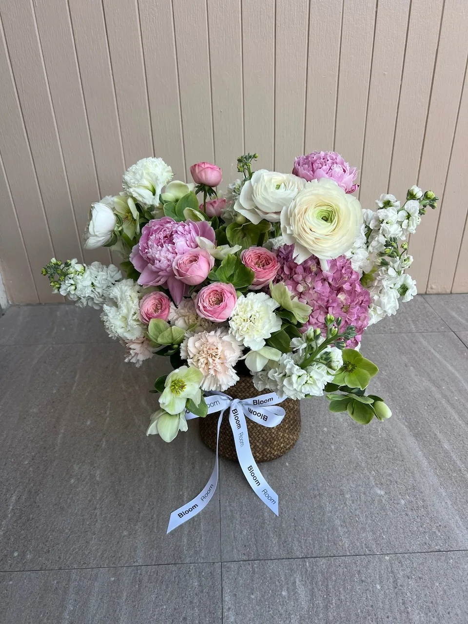Basket arrangement with pink hydrangeas, white ranunculus, pink spray roses and white blossoms