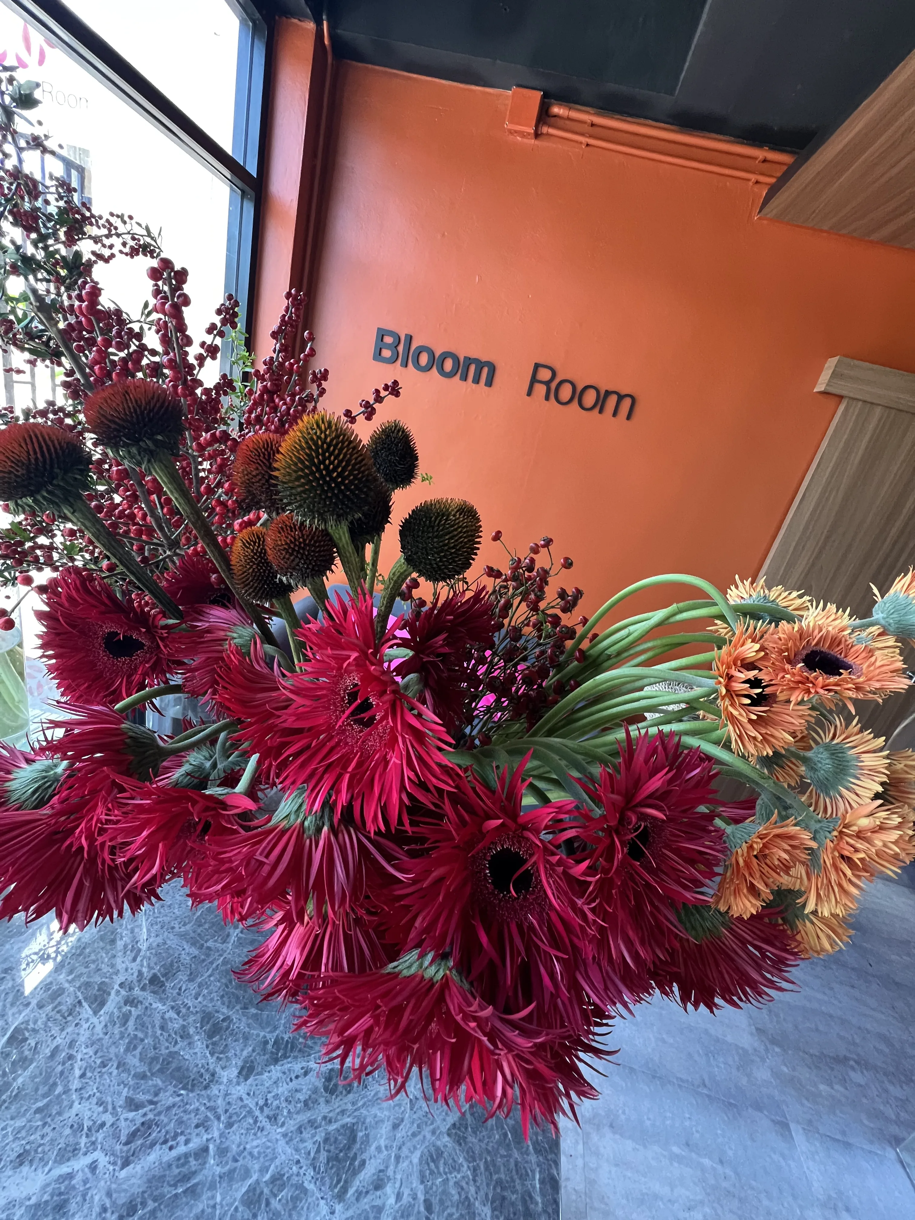 Dramatic wide arrangement of red spider gerberas, thistle and red berry branches against the Bloom Room wall.