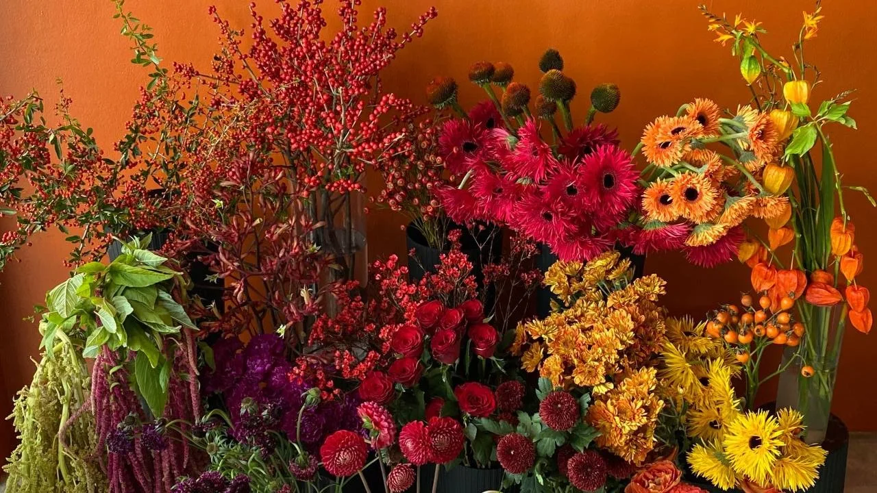 A Bloom Room Studio arrangement of tropical flowers, red berries, and seasonal blooms against a terracotta wall