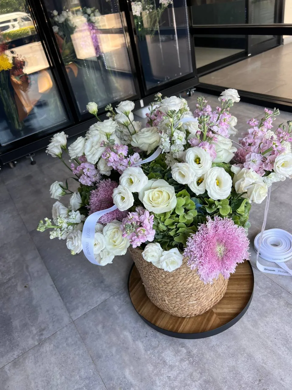 White lisianthus and pink pompom basket placed outside the Bloom Room storefront