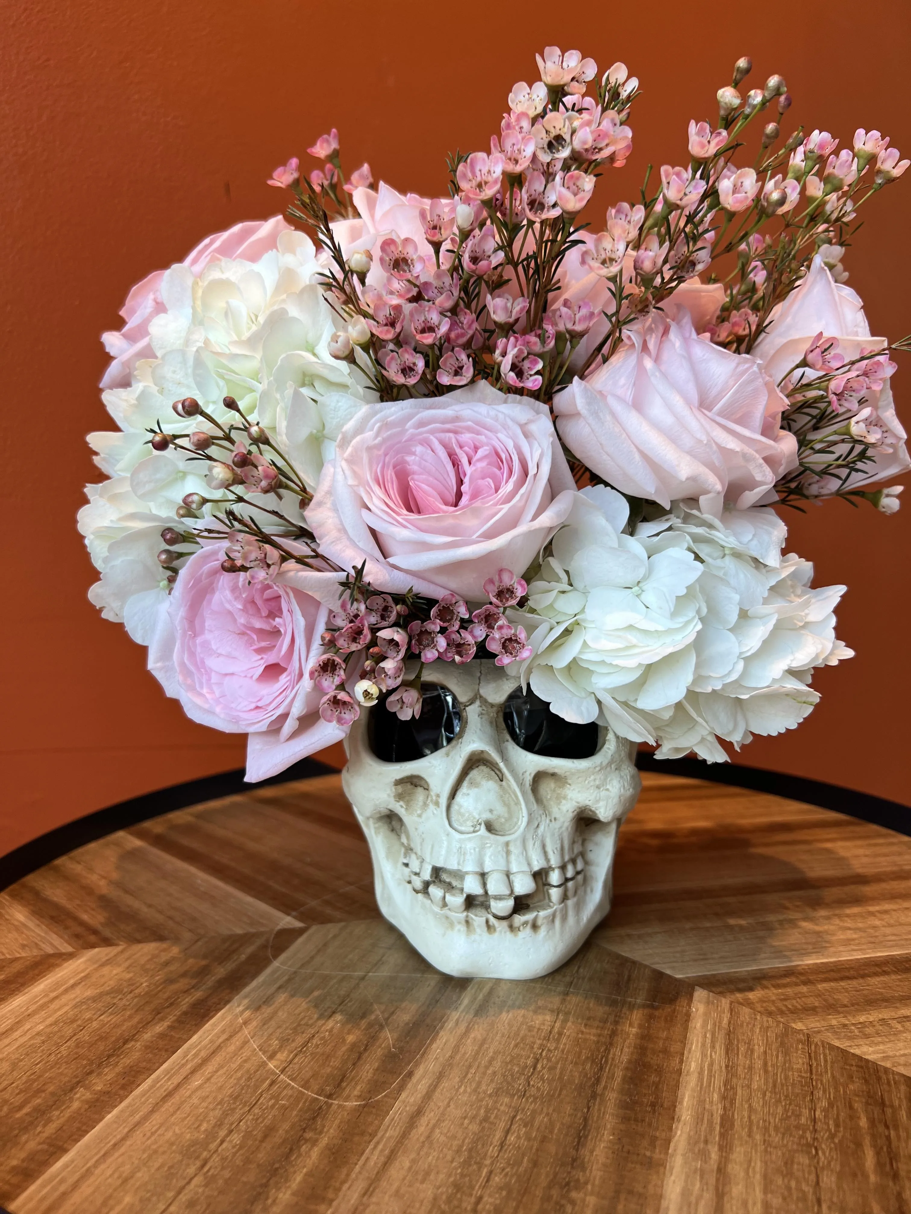 Pink garden roses and wax flower arranged in a white ceramic skull vase