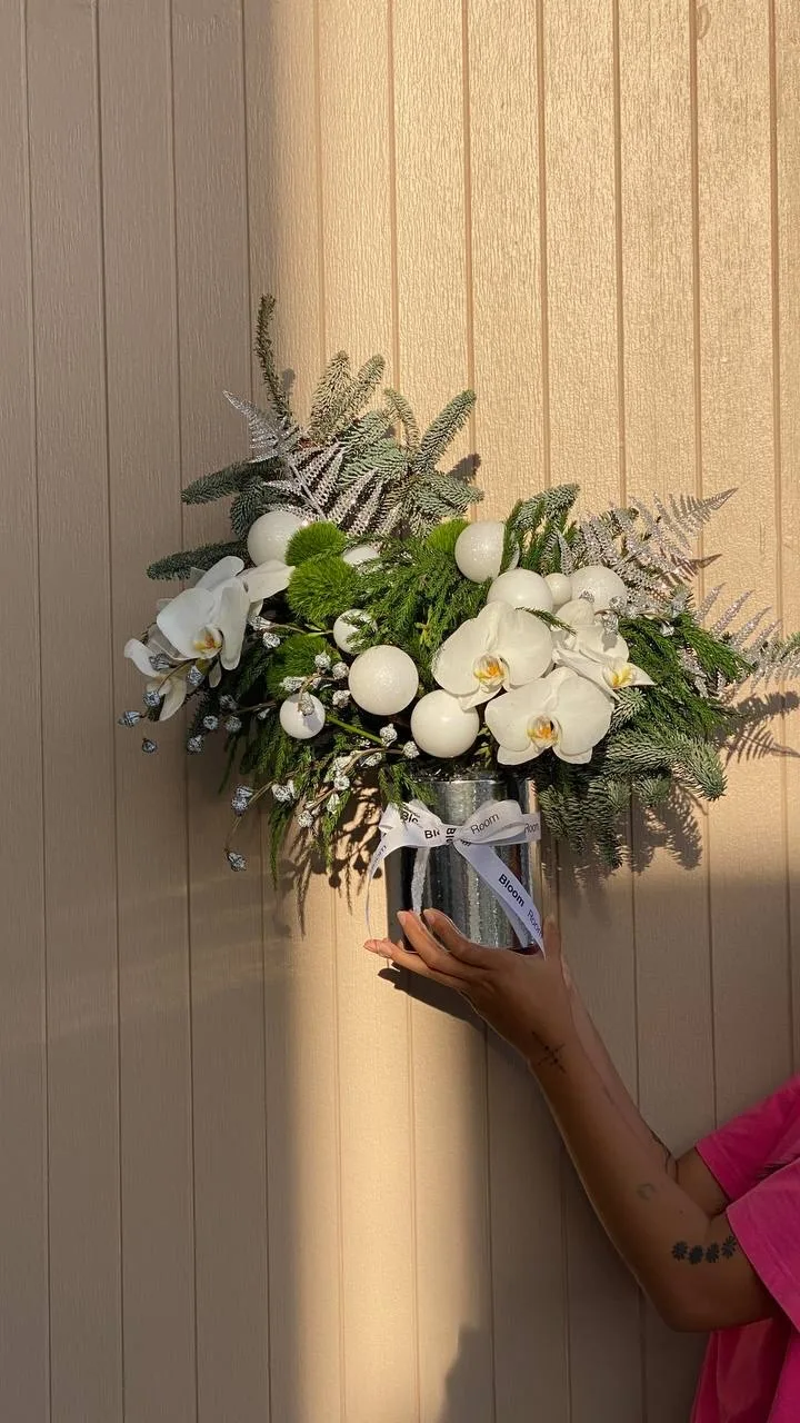White orchids, green dianthus and silver ornaments in a mirrored cylindrical box