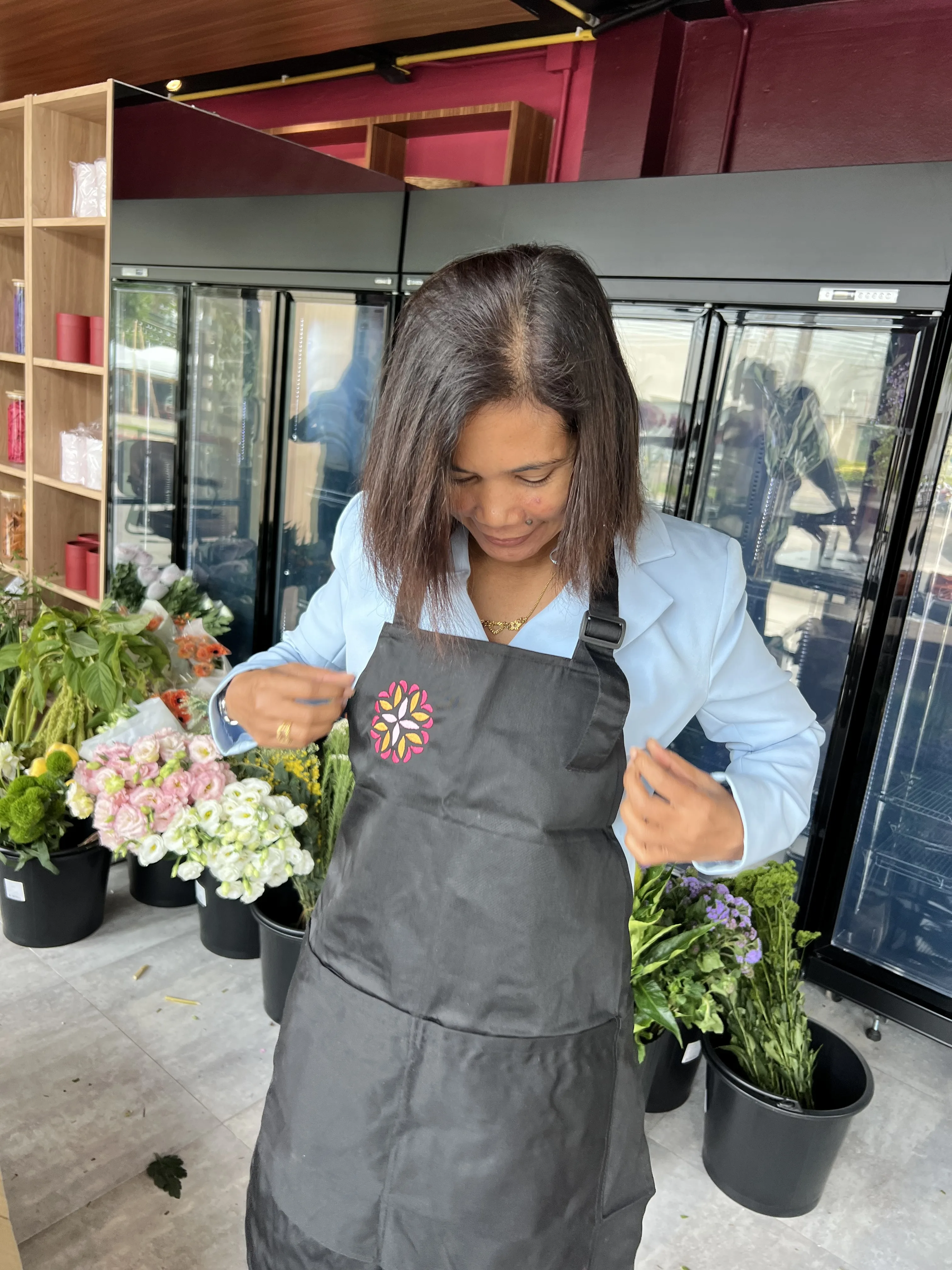 Florist in a Bloom Room apron smiles by the shop fridges.